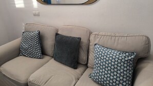 Un canapé beige agrémenté de trois coussins à motifs et d’un miroir rond dont le cadre est fait de fibres tressées.