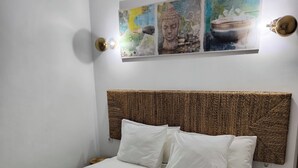 Un lit bien fait, recouvert d’une courtepointe blanche et turquoise à motifs, avec une tête de lit en osier et un luminaire fixé au mur.