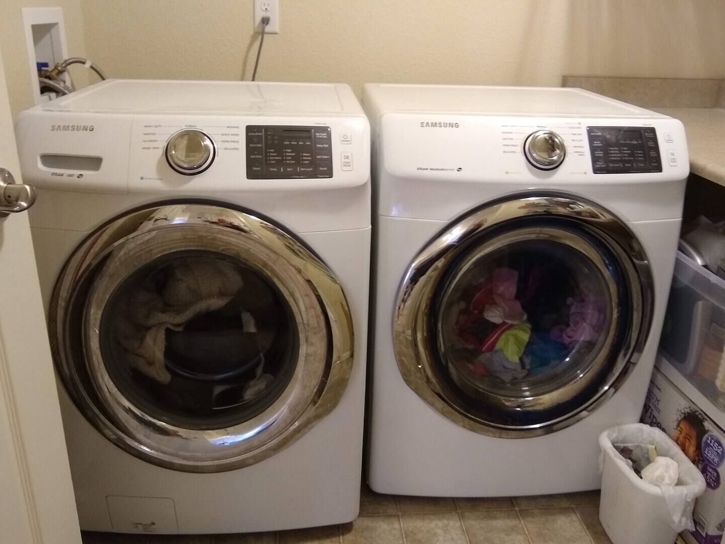 Two white Samsung front-loading washing machines in a laundry room.