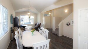 A dining area with a white table, chairs, and a vase of flowers. There is a piano and a staircase in the background. - Charming 4-bedroom home, High Speed Internet & AC in beautiful Colorado Springs (Colorado Springs)
