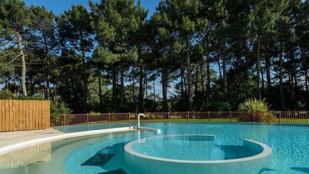 Une piscine de forme circulaire, entourée d’une terrasse en bois et d’une clôture.