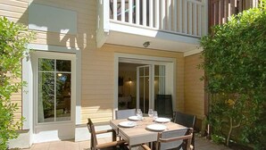 Une maison à deux étages avec un balcon, une terrasse dotée d’une table et de chaises, et une porte donnant sur l’intérieur.