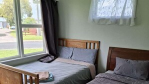 A room with two single beds, a wooden bench, a window with curtains, and a view of the outside. - 3 Bedroom House A 3 Frank St (Rotorua)