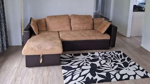A living room with a sectional sofa, a patterned rug, and a light-colored wooden floor. - 3 Bedroom House A 3 Frank St (Rotorua)