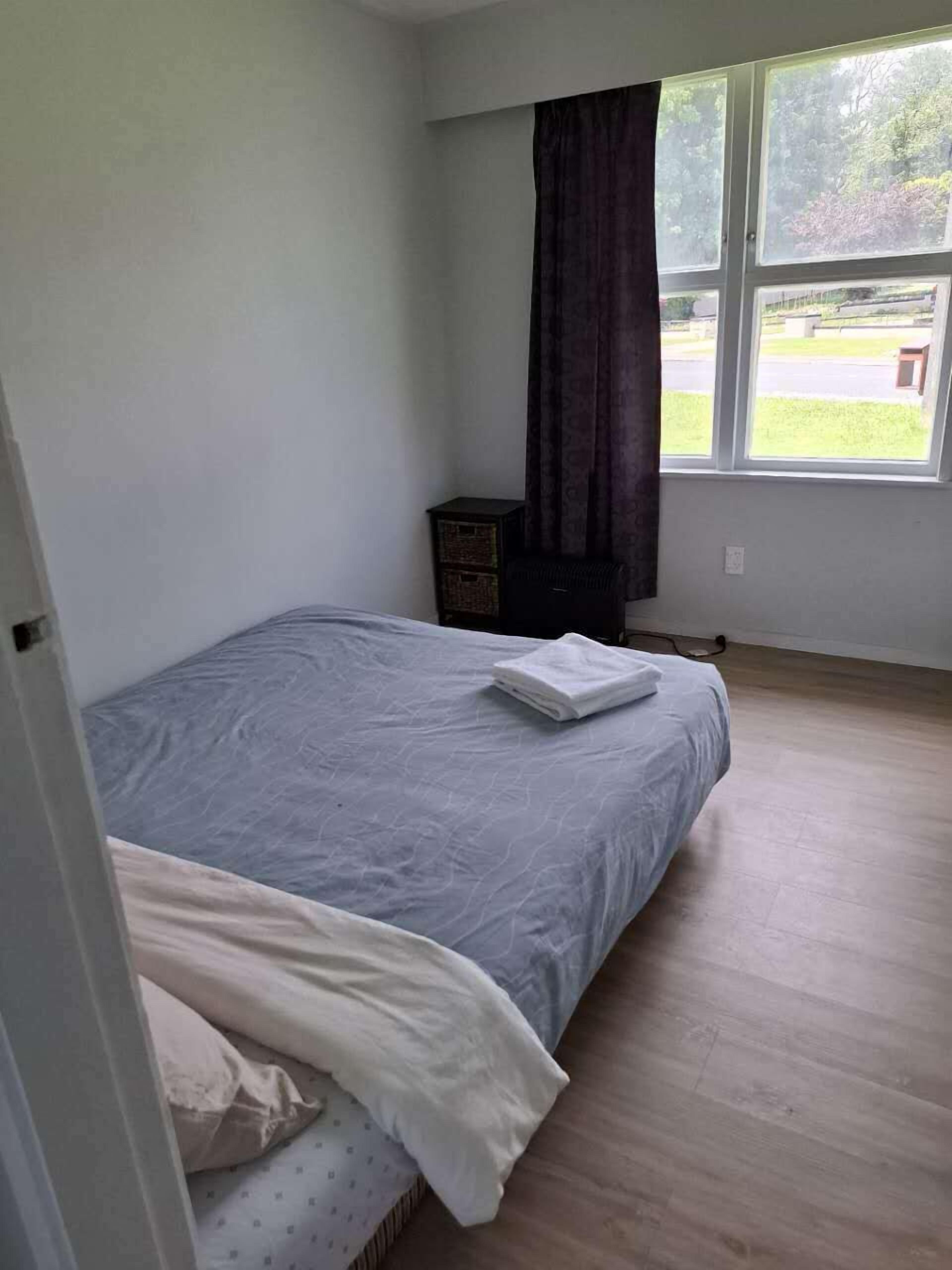 Un dormitorio con cama, ventana y un mueble pequeño.