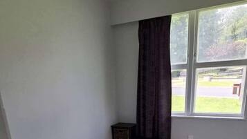 Un dormitorio con cama, ventana y un mueble pequeño.