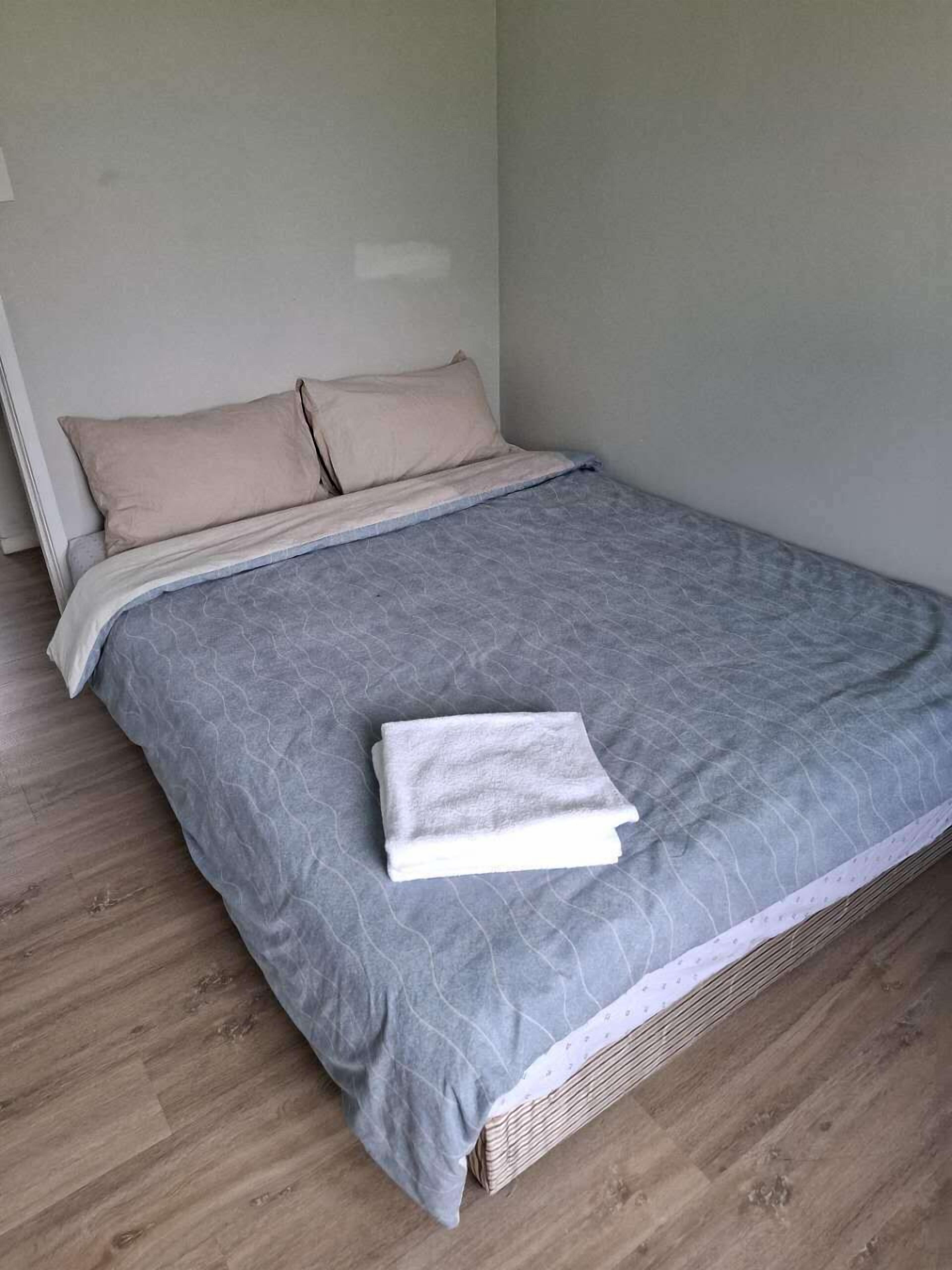 A neatly made bed with a grey bedspread and two beige pillows.