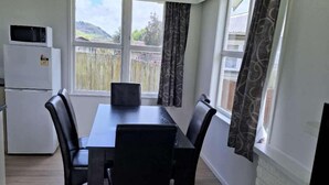 A dining area with a table and chairs, a refrigerator, and a window with curtains. - 3 Bedroom House A 3 Frank St (Rotorua)