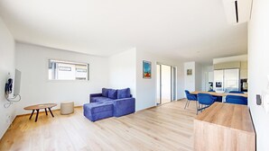 Ein modernes Wohnzimmer mit einem blauen Sofa, einem Holzesstisch und einer Küchenzeile im Hintergrund.