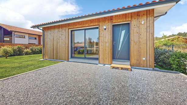 Ein modernes Haus mit Holzfassade, großen Schiebegläsern und einem Schotterweg.