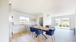 Eine moderne Küche mit Essbereich, ausgestattet mit einem Holztisch und blauen Stühlen, großen Fenstern und Blick ins Freie.