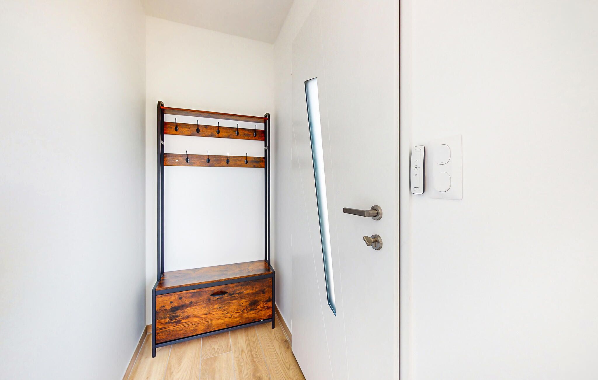A narrow hallway with a wooden bench, a door with a handle, and a light switch on the wall.