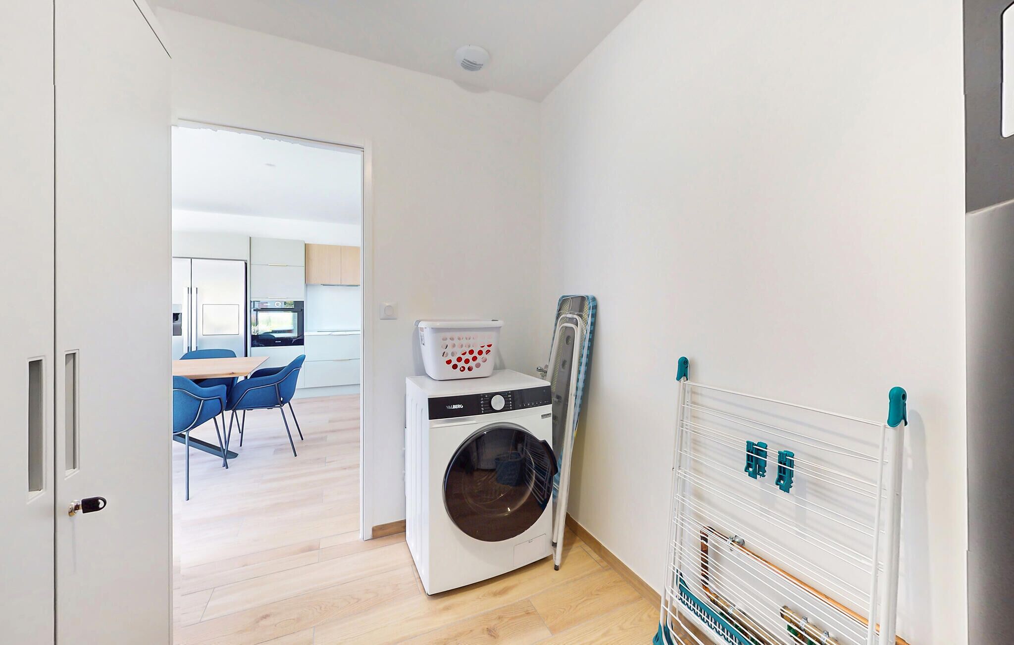 A compact apartment with a laundry area, a small kitchen, and a dining area with blue chairs.