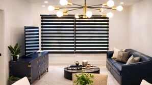Ein modernes Wohnzimmer mit einem Glastisch, zwei Sofas, einem dunkelblauen Schrank und einer schwarz-weiß gestreiften Wand.