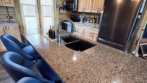 Una cocina con encimeras de granito, refrigerador de acero inoxidable y gabinetes de madera.