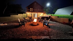 Un rincón al aire libre acogedor, con sillas Adirondack y un brasero, rodeado por un patio de grava.