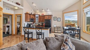 A modern kitchen with wooden cabinets, a central island with bar stools, and a dining area with a view. - Estes Park Retreat w/ Views, Heated Pool, Minutes to Town (Estes Park)