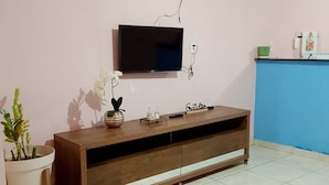 A living room with a TV mounted on the wall, a wooden cabinet, a potted plant, and a blue wall. - Cozy house for family. (Lagoa Seca Juazeiro do Norte)