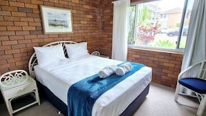 A hotel room with a bed, a nightstand, a chair, a ceiling fan, and a window with curtains.