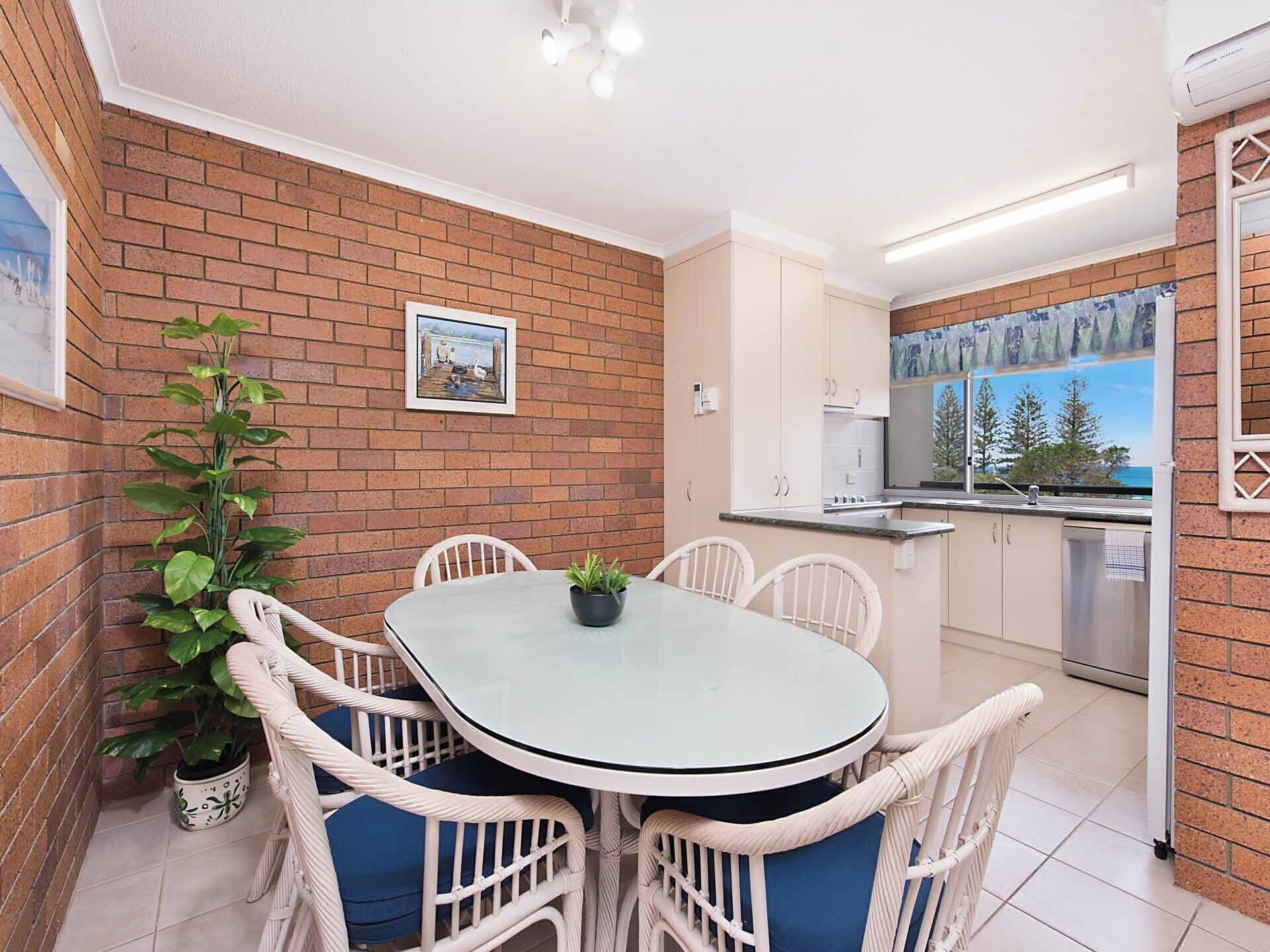 Una cocina compacta con zona de comedor, que presenta una pared de ladrillo, una planta en maceta y vistas a través del ventanal.