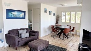 A living room with a sofa, a coffee table, a dining table with chairs, a TV, and artwork on the walls.