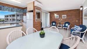 A modern apartment with a kitchen, dining area, and living room. It features a balcony with a view, a refrigerator, a dining table with chairs, and a small potted plant.