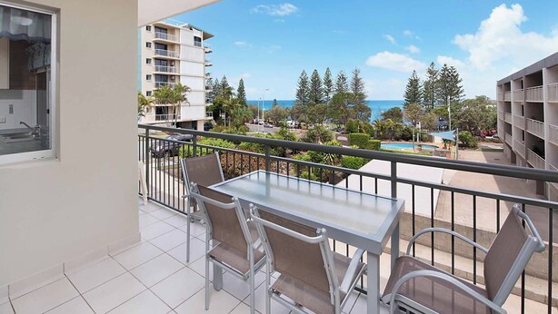 A balcony with a table and chairs, overlooking a pool and buildings.