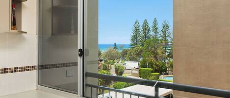 A kitchen with a sliding glass door leading to a balcony with a view of the ocean and trees.