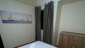 A neatly made bed with white linens and a rolled towel, a wooden wardrobe, and a painting of sailboats on the wall. - Refúgio das Dunas, perfect for those who collect moments with family/friends. (Capim Macio Natal)