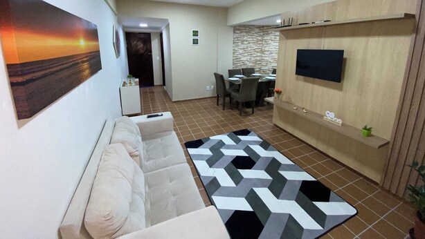 A living room with a sofa, a TV mounted on the wall, a dining area with a table and chairs, and a hallway leading to a door. - Refúgio das Dunas, perfect for those who collect moments with family/friends. (Capim Macio Natal)