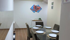 A dining area with a glass table set for six, surrounded by chairs. There is a decorative painting on the wall above the table. - Refúgio das Dunas, perfect for those who collect moments with family/friends. (Capim Macio Natal)