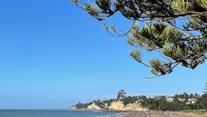 Uma praia com pessoas caminhando, céu claro e edifícios ao fundo.