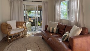 Uma sala de estar com sofá de couro marrom, poltrona de vime e porta de vidro que dá para uma área externa.