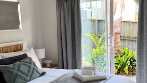 Cama bem arrumada com lençóis brancos, um cobertor cinza e duas toalhas dobradas.