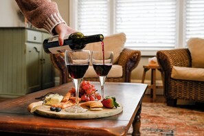 A dining table with a bottle of wine being poured into glasses, a plate with cheese, crackers, grapes, and a strawberry. - Carisbrook Cottage is a beautiful, cosy, pet friendly home 2 blocks from the CBD (Armidale)