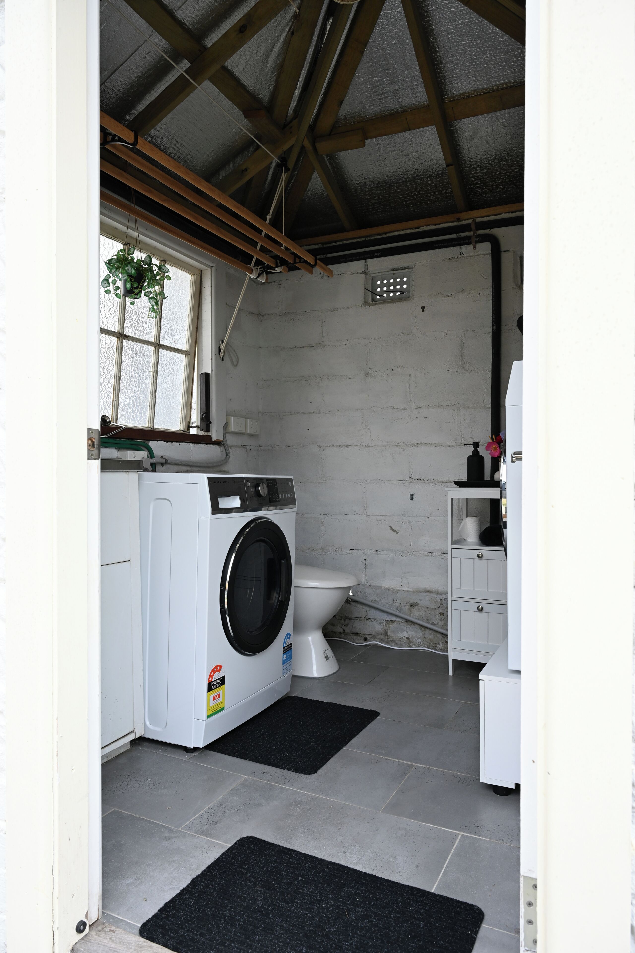 A laundry room with a washing machine, a toilet, and a small cabinet.