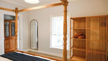 Une chambre à coucher avec un lit à baldaquin, une armoire en bois, un grand miroir et une fenêtre avec des stores.