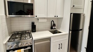 A modern kitchen with white cabinets, a stainless steel stove, a black refrigerator, and a built-in microwave.