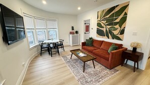 A living room with a brown sofa, a coffee table, a TV mounted on the wall, and a large abstract painting.
