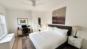 A bedroom with a large bed, a desk, a chair, a wardrobe, and a ceiling fan.