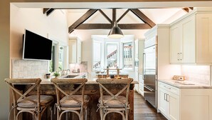 A kitchen with a central island, bar stools, a TV, and a large window.