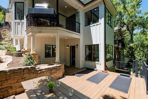 Une maison moderne à deux étages dotée d’une terrasse, d’un espace salon extérieur et d’un mur de soutènement en pierre.