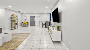 Un salon moderne avec un canapé blanc, une table basse, un téléviseur fixé au mur et un coin repas comprenant des chaises et une table.