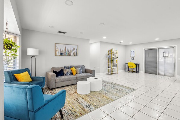 A modern living room with a grey sofa, blue armchair, and a patterned rug. - Cozy 3BR Vero Beach Retreat 10 Mins to Beaches. Early Check-In & Late Check-Out! (Vero Beach)