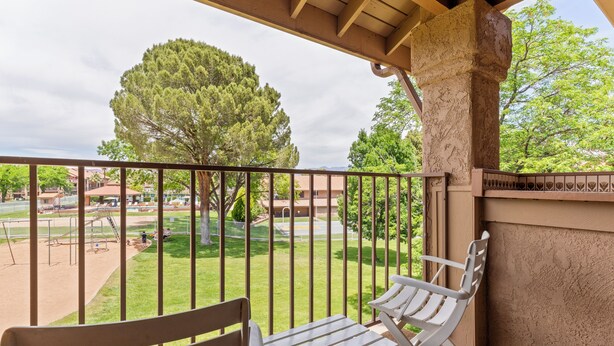 A balcony with two white chairs and a wooden bench, overlooking a playground and a building with a green lawn. - Open Two-level/3 bdrm/Sleeps 16/Pools & Hot Tubs/Mini-Golf/Family friendly! (St. George)