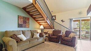 A living room with a beige sofa, patterned armchairs, a wooden staircase, and a large window with a view of the outdoors. - Open Two-level/3 bdrm/Sleeps 16/Pools & Hot Tubs/Mini-Golf/Family friendly! (St. George)