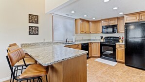 A kitchen with a granite countertop, wooden cabinets, a black refrigerator, and a built-in oven. - Open Two-level/3 bdrm/Sleeps 16/Pools & Hot Tubs/Mini-Golf/Family friendly! (St. George)