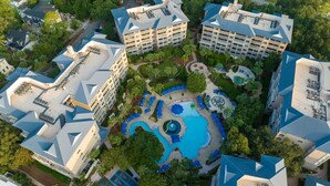 A hotel complex with multiple buildings, a central swimming pool area, and surrounding greenery.