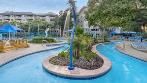 A swimming pool with a dolphin sculpture, lounge chairs, and a tropical garden setting.
