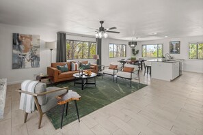 A spacious living area with a sofa, coffee table, and chairs, a dining area with a table and chairs, and a kitchen with a sink and island.